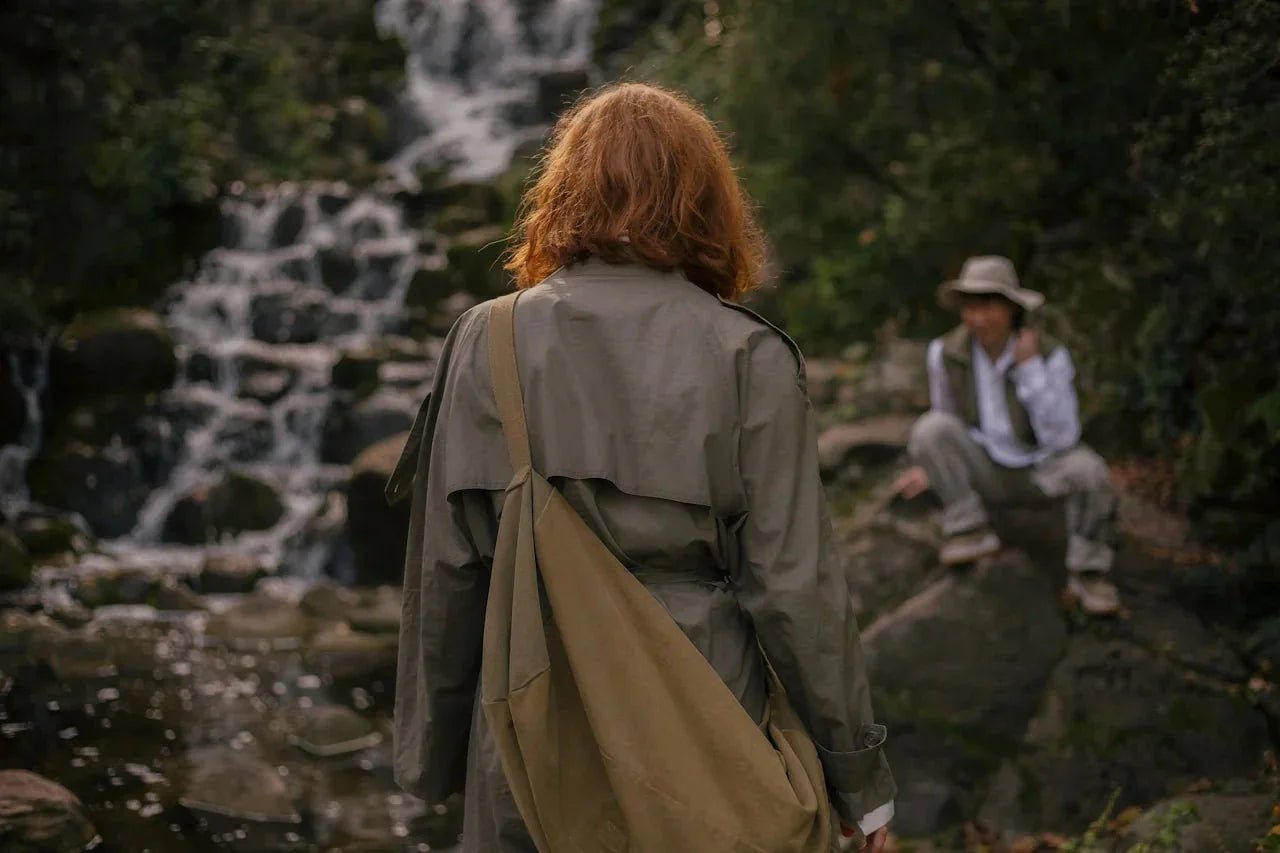 Two people in a forest by a small waterfall, pausing to talk and observe the surroundings