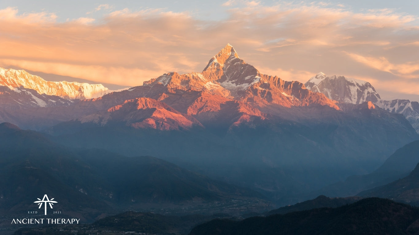 Sunset over snow-capped himalayan mountains with 'Ancient Therapy' logo in the corner.