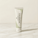 A tube of Ancient Therapy Recovery Balm standing upright on a light marble surface against a warm off-white background.