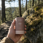 Person som håller en Ancient Therapy Chaga-burk på en mossig klippa i en skog