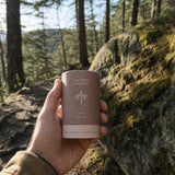 Person som håller en Ancient Therapy Chaga-burk på en mossig klippa i en skog